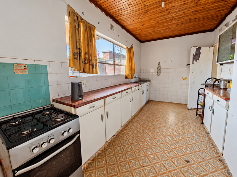 A dated kitchen featuring a gas stove, timber ceiling, and original cabinetry, offering significant potential for a modern renovation.