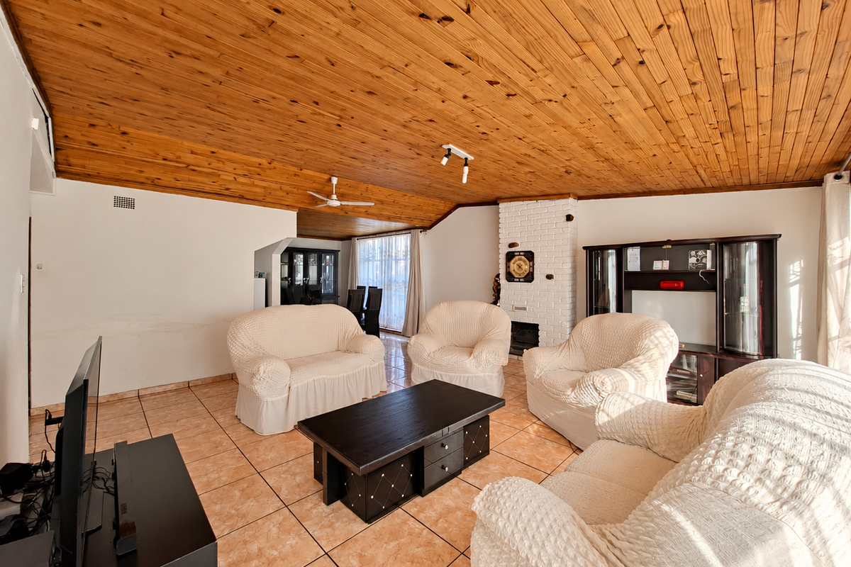 Spacious living room featuring a vaulted timber-clad ceiling, ceramic tiled flooring, and a classic brick fireplace, offering a warm and traditional aesthetic.