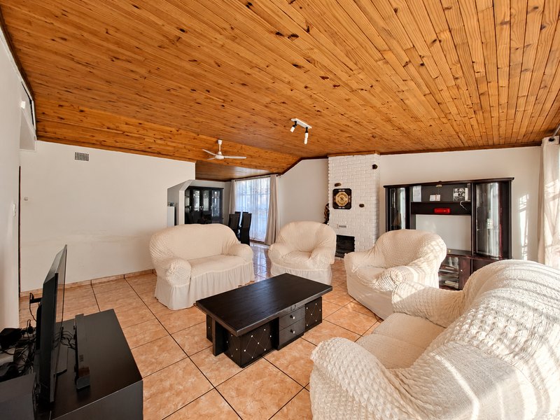 Spacious living room featuring a vaulted timber-clad ceiling, ceramic tiled flooring, and a classic brick fireplace, offering a warm and traditional aesthetic.