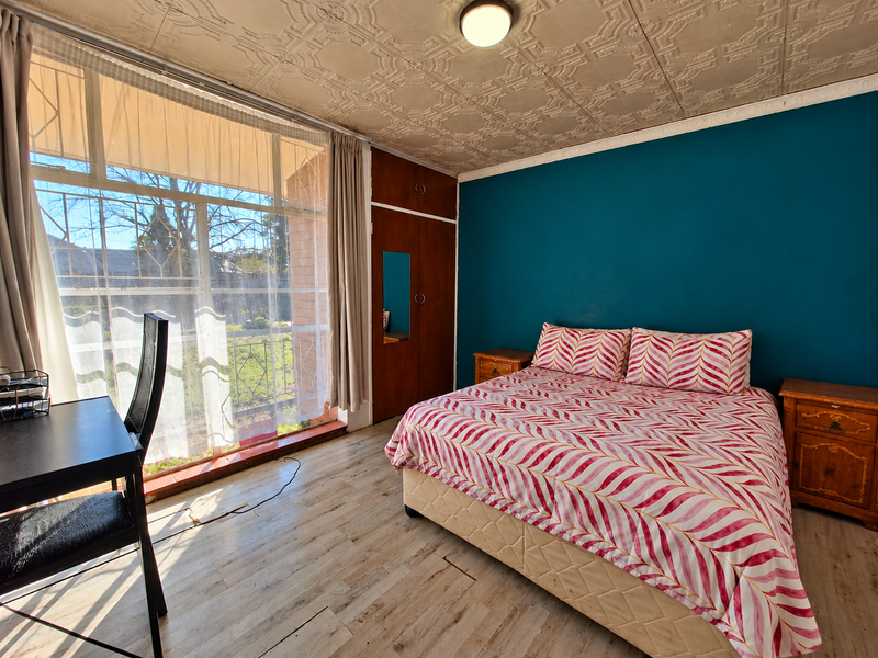 A bedroom featuring a built-in wardrobe, textured ceiling tiles, and large windows allowing natural light, with laminate flooring throughout.