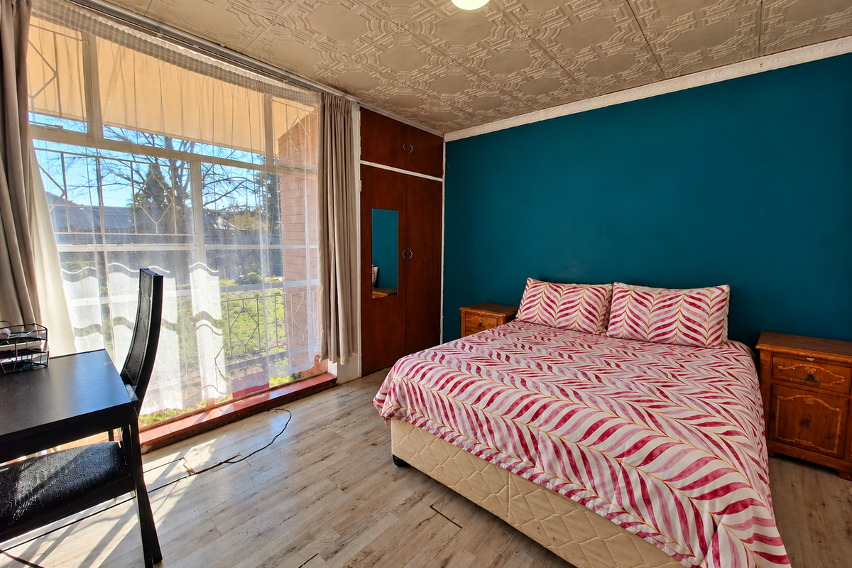 A bedroom featuring a built-in wardrobe, textured ceiling tiles, and large windows allowing natural light, with laminate flooring throughout.