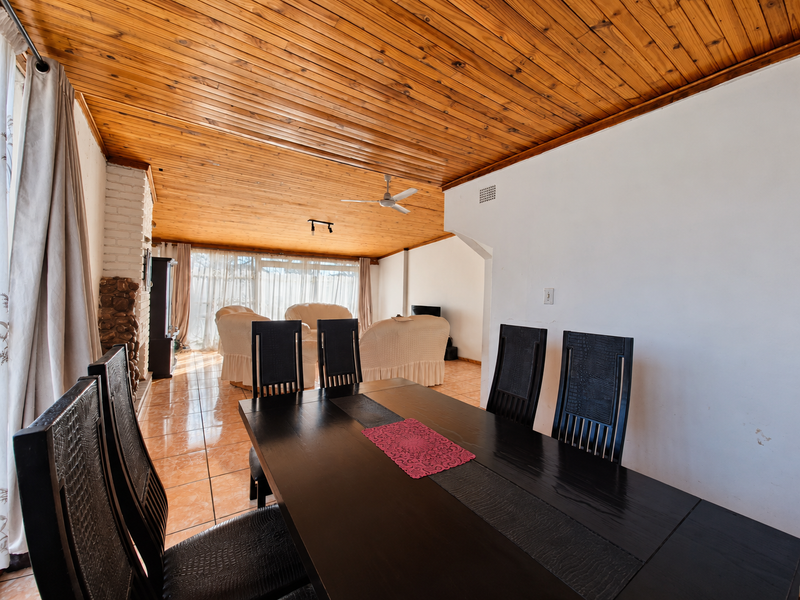 Open plan living and dining area featuring a distinctive timber tongue and groove ceiling, ceramic tiled flooring, and a brick fireplace.