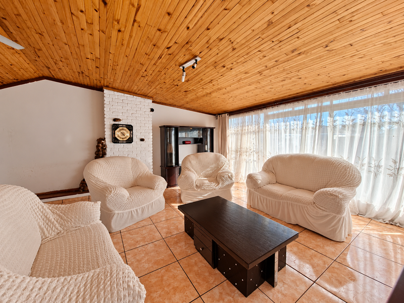 Spacious living room featuring a distinctive timber tongue and groove ceiling, a brick fireplace, and ceramic tiled flooring with large windows.