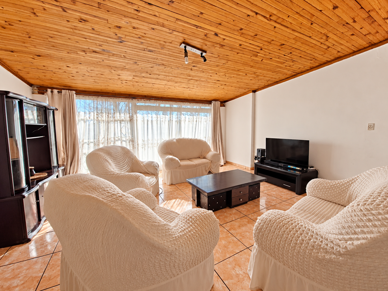 A spacious living room featuring a warm timber-clad ceiling, tiled flooring, and large sliding glass doors that provide ample natural light.