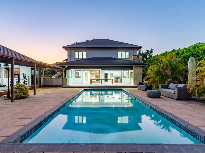 A well-maintained outdoor pool area featuring a tiled deck, covered patio space, and seamless indoor-outdoor flow through large sliding glass doors.