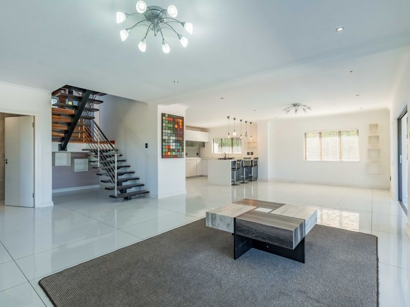 Spacious open-plan living area featuring polished tiled floors, a modern floating staircase with metal balustrades, and a sleek kitchen with a central island.