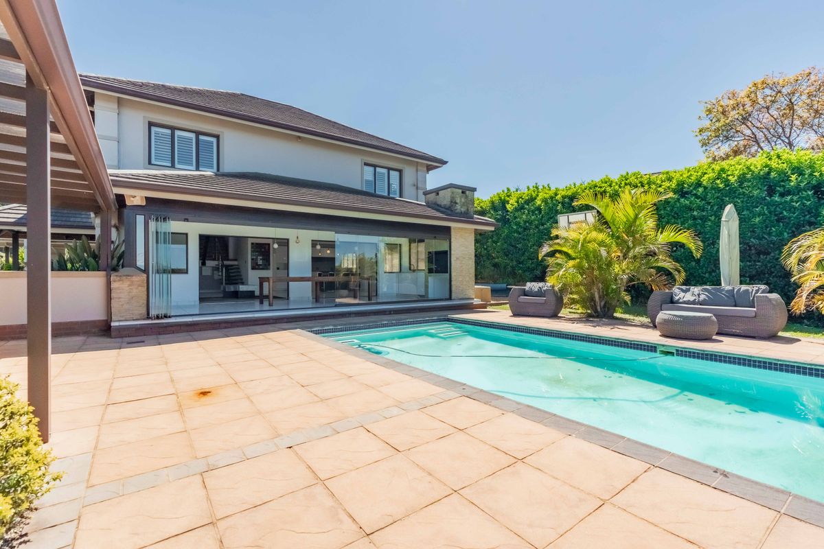 Rear exterior view featuring a swimming pool, spacious tiled patio, and large stacking glass doors providing seamless indoor-outdoor flow.