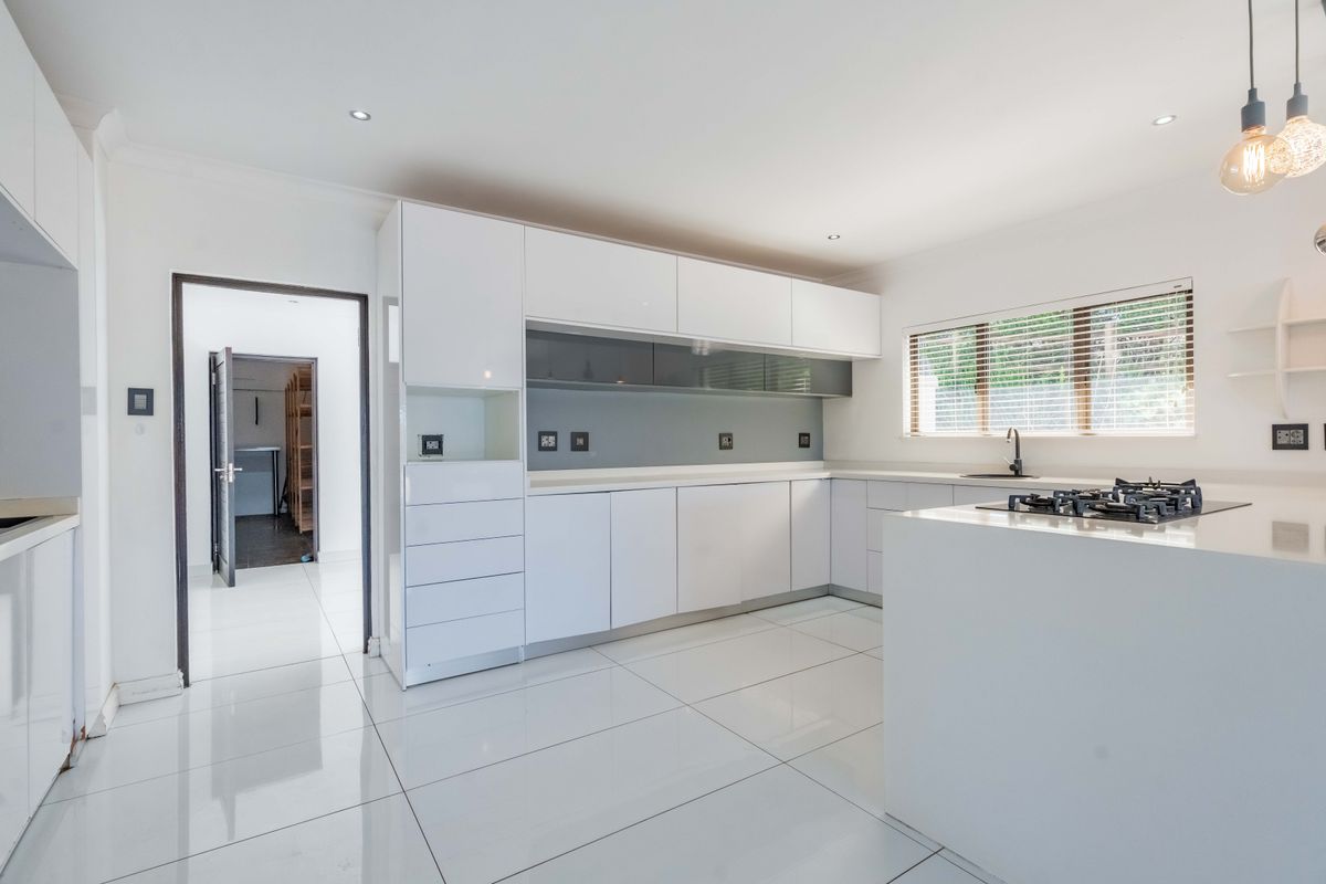 Modern kitchen featuring white high-gloss cabinetry, stone countertops, a gas hob, and sleek tiled flooring, offering a clean and contemporary aesthetic.