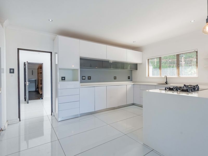 Modern kitchen featuring white high-gloss cabinetry, stone countertops, a gas hob, and sleek tiled flooring, offering a clean and contemporary aesthetic.
