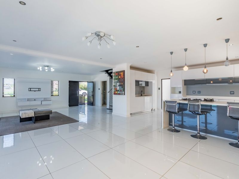 Spacious open-plan living area featuring high-gloss porcelain tiles, a modern kitchen with a central island, gas hob, and integrated appliances, flowing into the lounge.