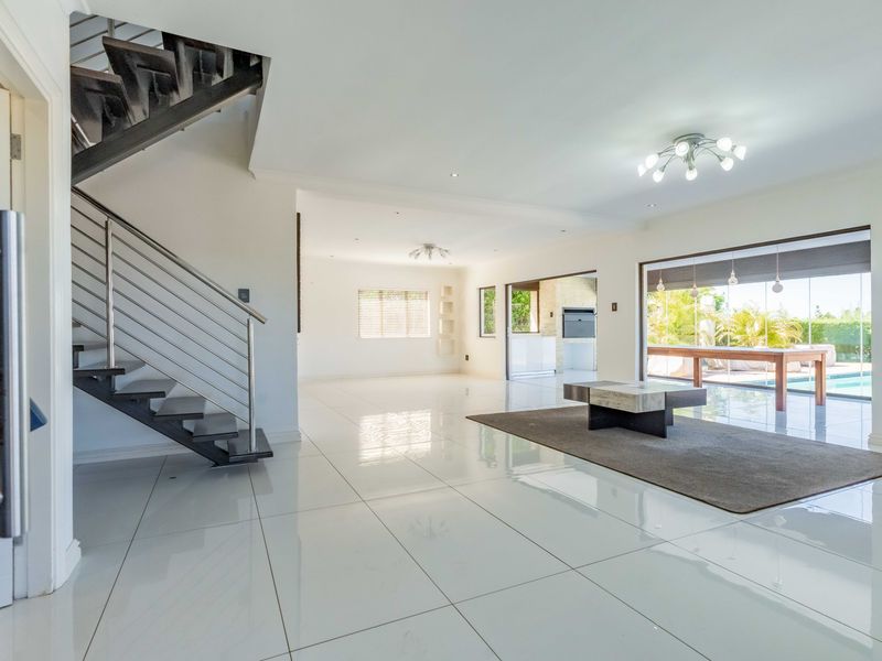 Spacious open-plan living area featuring polished porcelain tiles, a modern staircase with stainless steel balustrades, and seamless flow to the outdoor patio and pool.