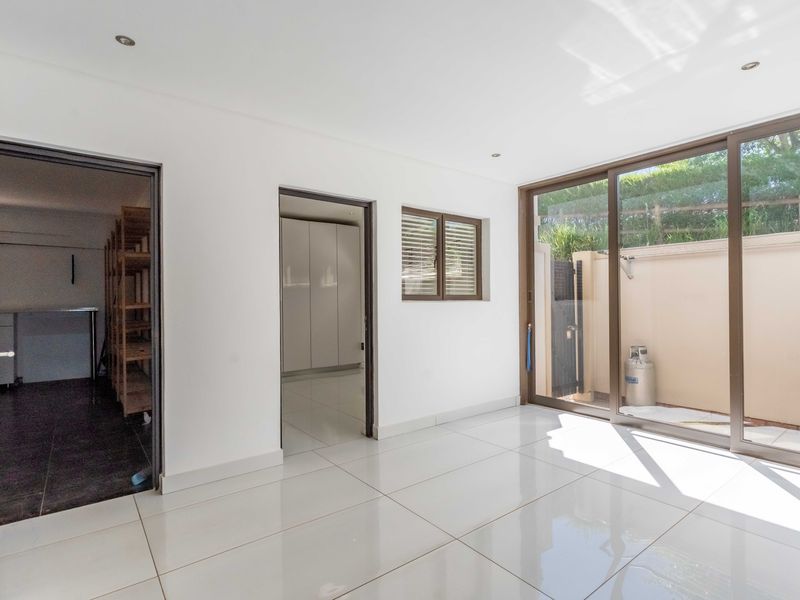 A bright, empty living area featuring large sliding glass doors, modern tiled flooring, and recessed downlights, providing direct access to an outdoor space.