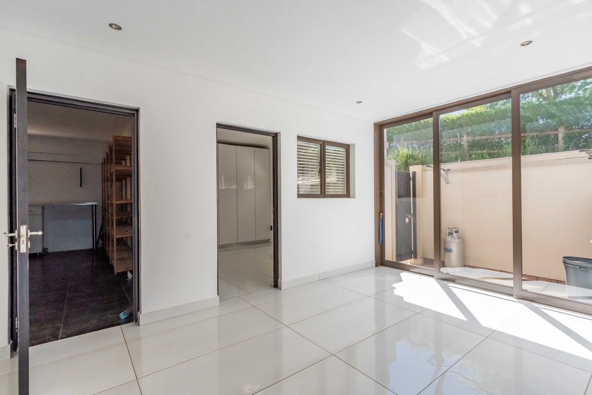 A bright, empty living area featuring large sliding glass doors, modern tiled flooring, and recessed downlights, providing direct access to an outdoor space.