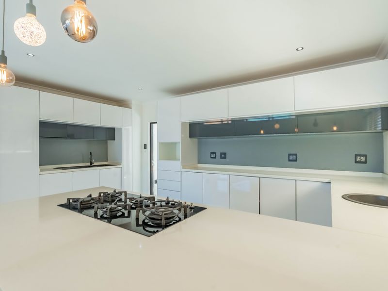 Modern kitchen featuring sleek white cabinetry, stone countertops, a central gas hob, and high-quality integrated finishes in a clean, minimalist design.