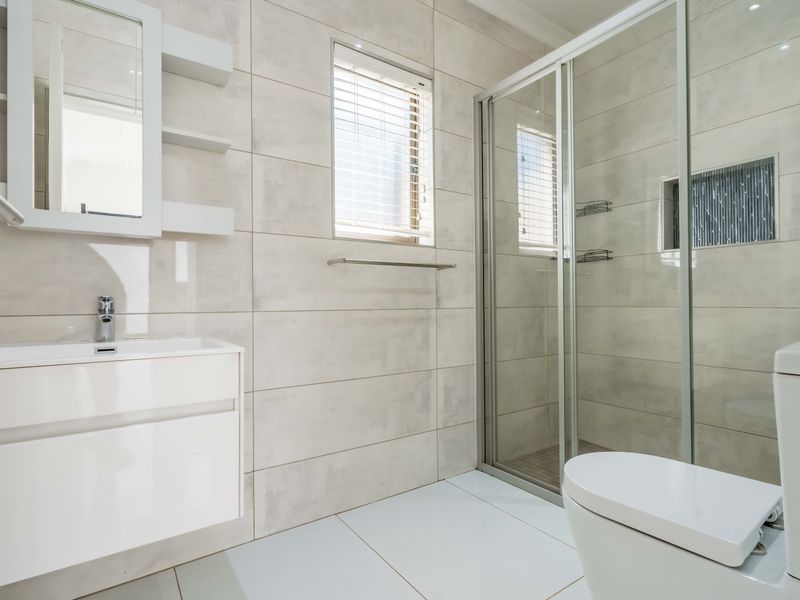 A modern, well-maintained bathroom featuring a sleek vanity, a glass-enclosed shower with a recessed niche, and neutral large-format wall and floor tiles.
