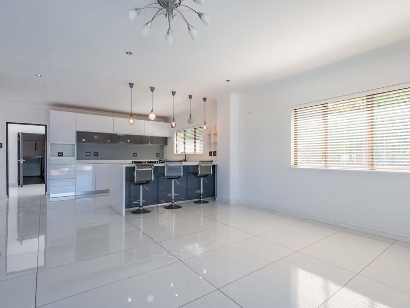 Modern open-plan kitchen featuring a central island, sleek cabinetry, high-gloss floor tiles, and contemporary lighting, creating a bright and spacious living environment.