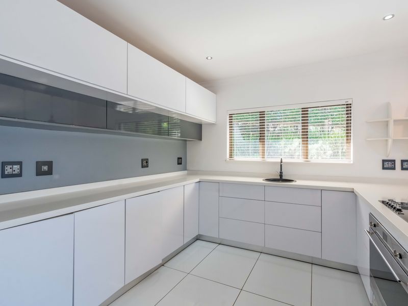 Modern, minimalist kitchen featuring sleek white cabinetry, stone countertops, integrated gas hob, built-in oven, and high-quality tiled flooring.