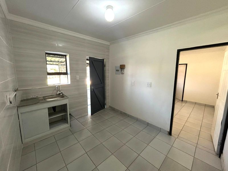 A functional kitchen area featuring tiled walls and flooring, a stainless steel sink, and direct access to an adjacent room.