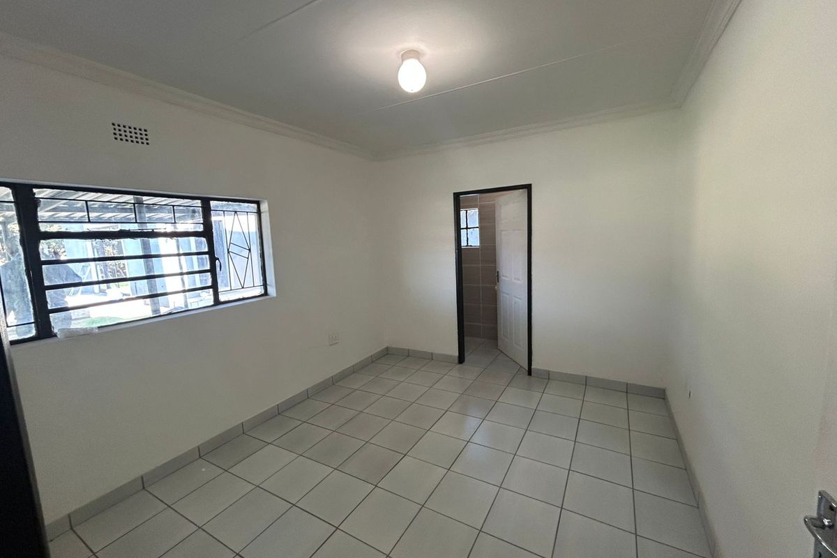 A clean, empty bedroom featuring neutral tiled flooring, security bars on the window, and a simple ceiling light fixture.