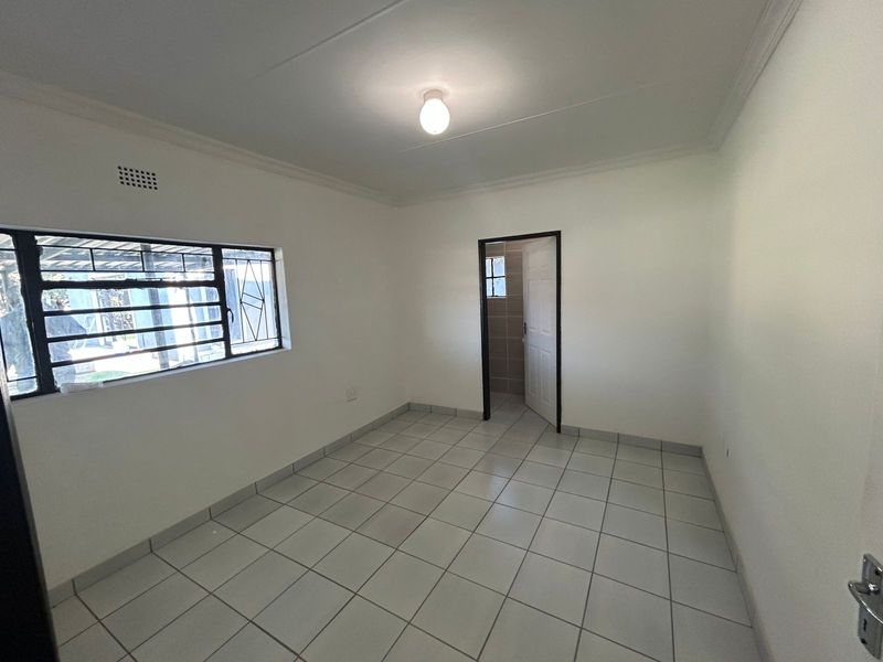 A clean, empty bedroom featuring neutral tiled flooring, security bars on the window, and a simple ceiling light fixture.