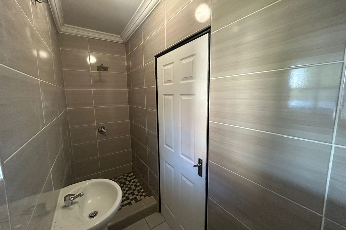 A clean, modern bathroom featuring neutral wall tiles, a pedestal basin, and a walk-in shower area with contemporary fixtures.