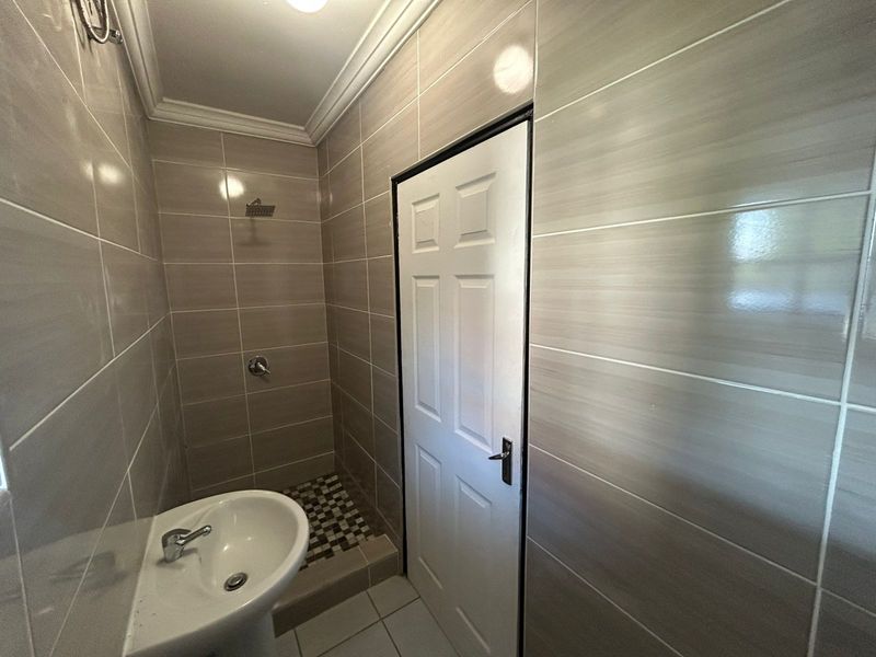 A clean, modern bathroom featuring neutral wall tiles, a pedestal basin, and a walk-in shower area with contemporary fixtures.