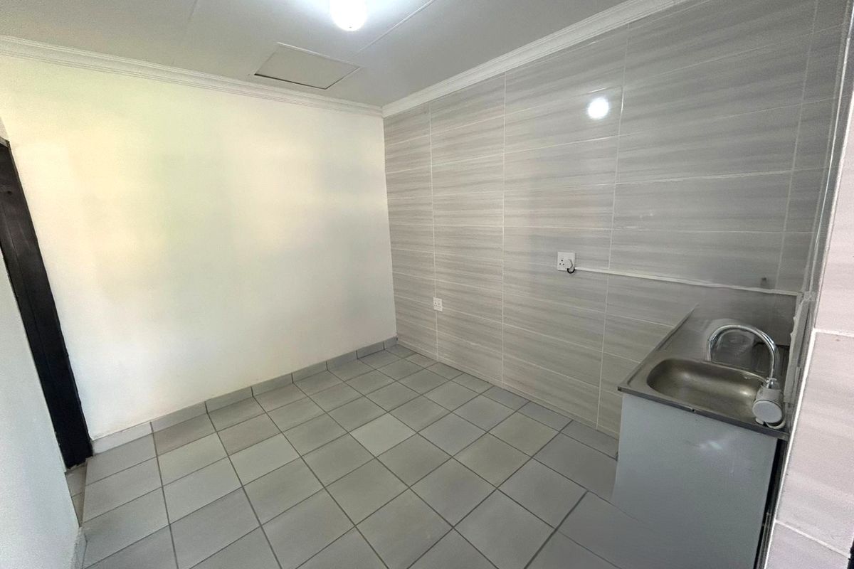 A functional, empty kitchen area featuring tiled flooring, a tiled wall splashback, and a stainless steel sink unit.
