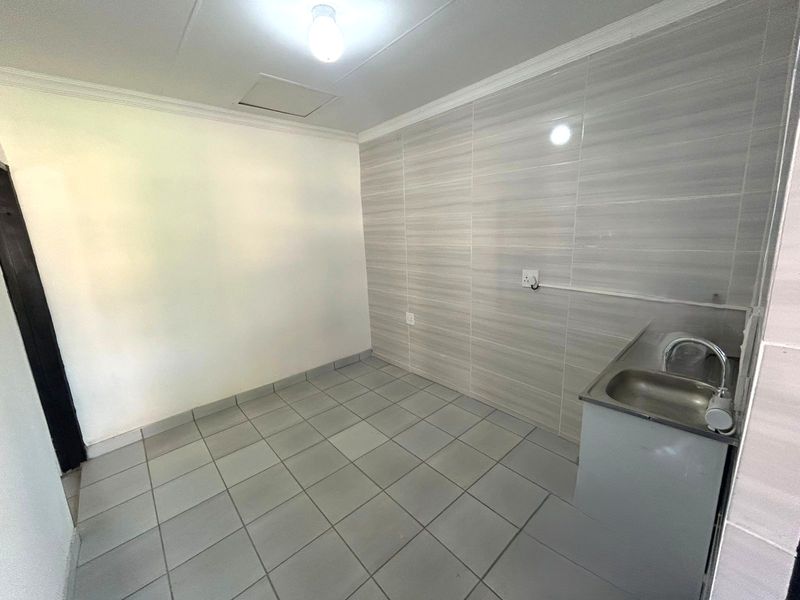 A functional, empty kitchen area featuring tiled flooring, a tiled wall splashback, and a stainless steel sink unit.