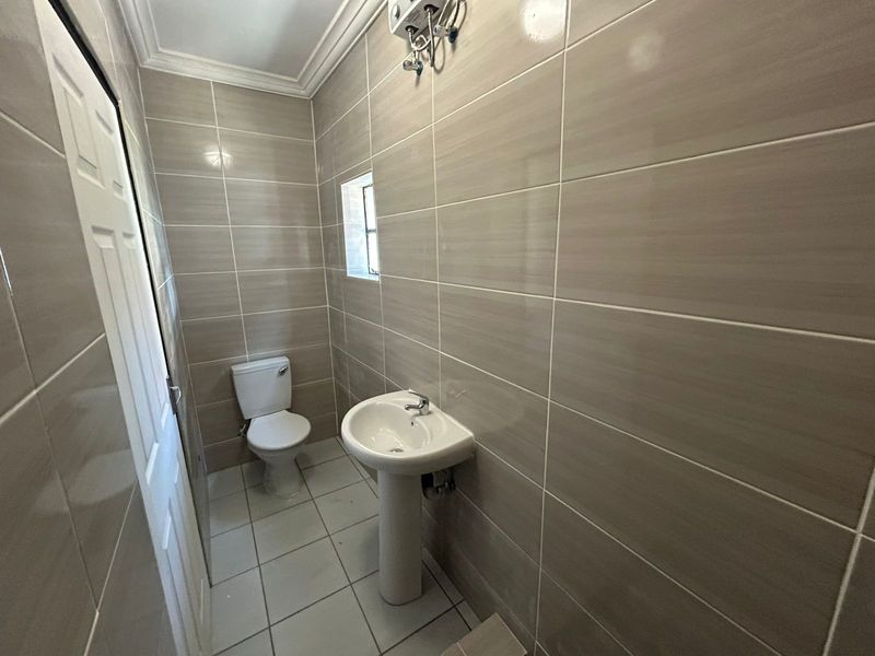 A clean and functional bathroom featuring neutral ceramic wall and floor tiles, a pedestal basin, and a standard toilet.