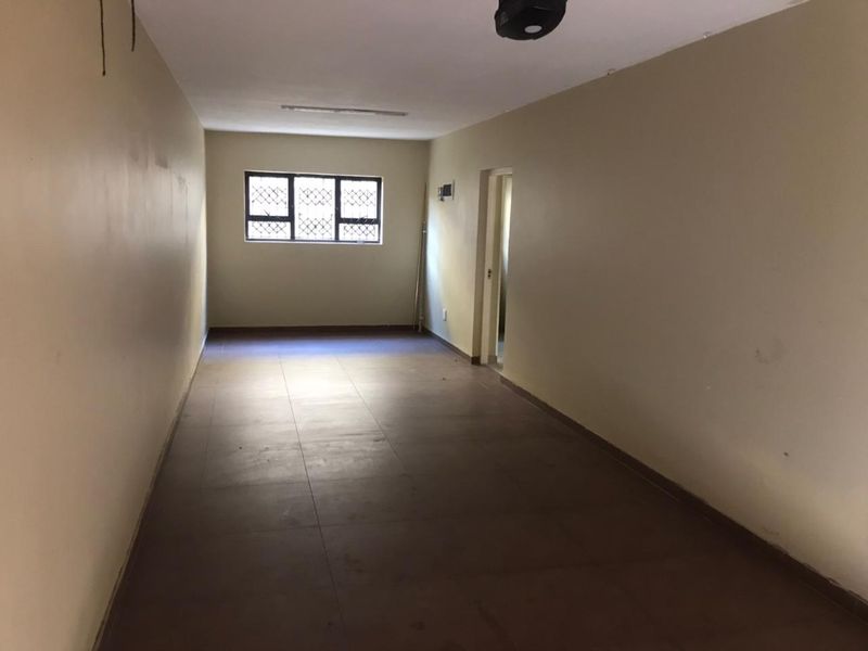 An empty, rectangular living area featuring tiled flooring and a window with security bars, offering a blank canvas for interior design.