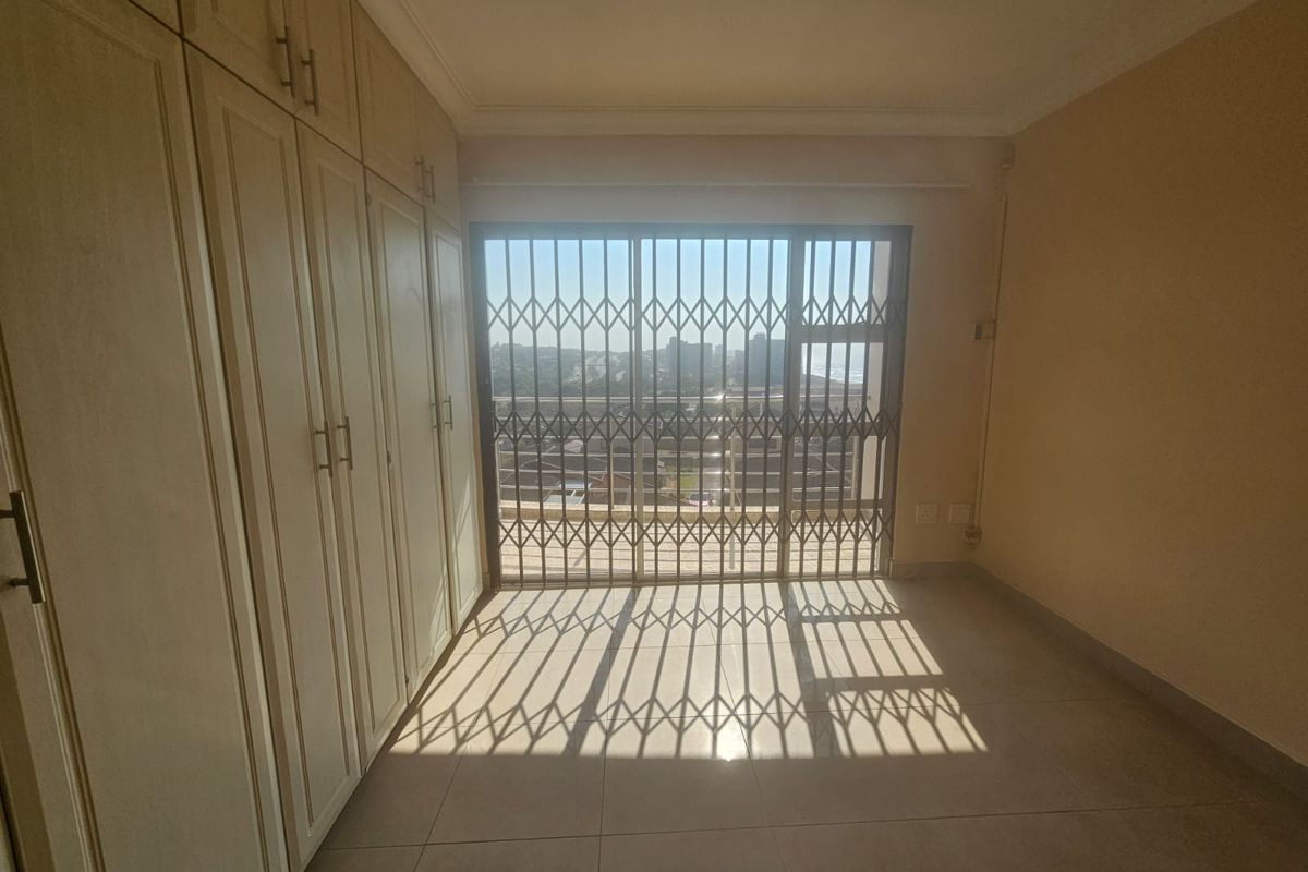 An empty bedroom featuring extensive built-in cupboards, tiled flooring, and a sliding door with a security gate leading to an outdoor area.