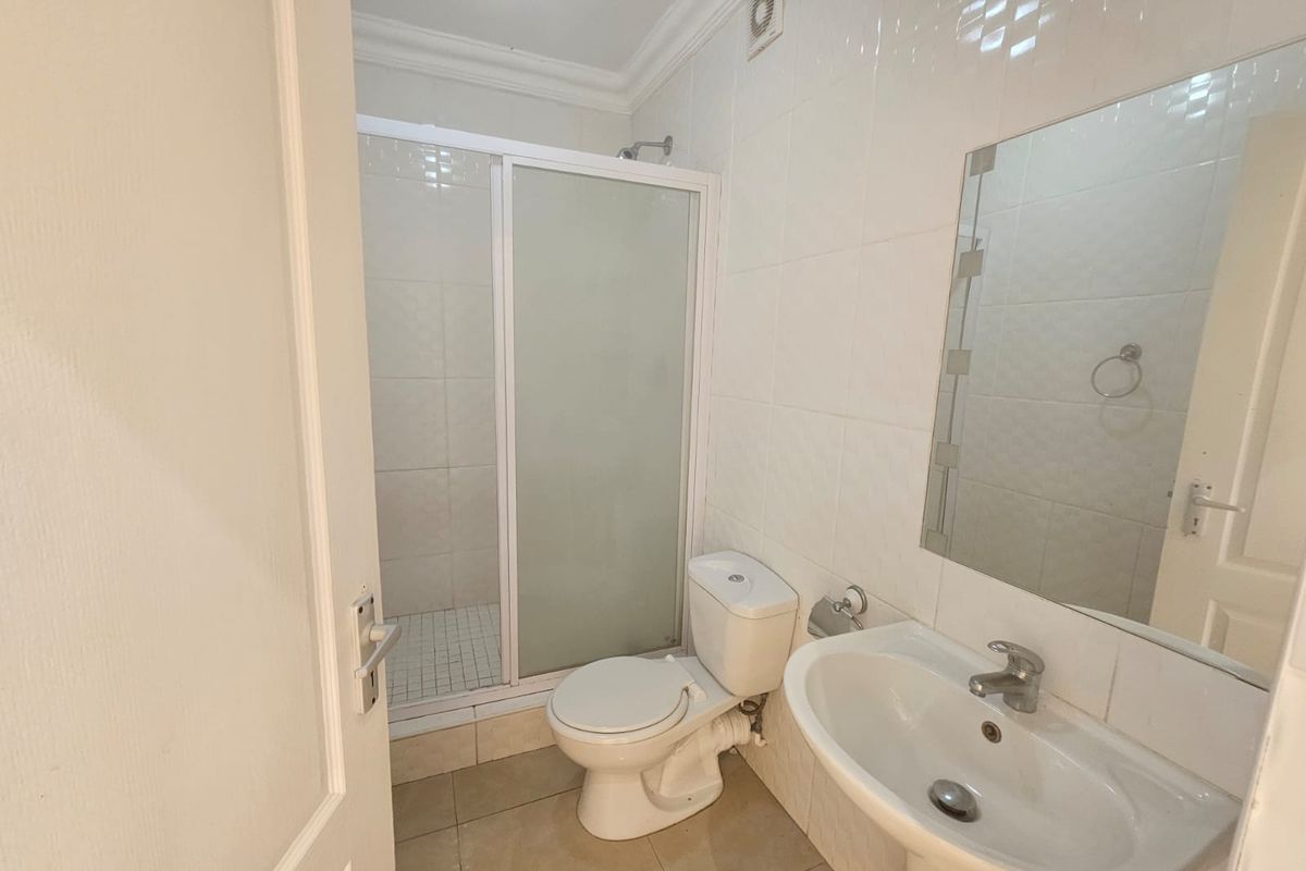 A functional bathroom featuring a shower enclosure, pedestal basin, and toilet, finished with neutral wall and floor tiles.