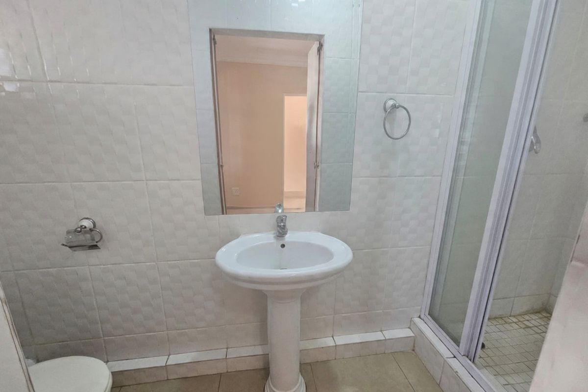 A functional bathroom featuring a pedestal basin, wall-mounted mirror, and a separate shower enclosure with tiled finishes throughout.