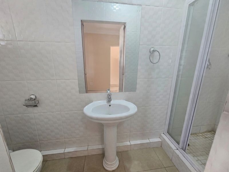 A functional bathroom featuring a pedestal basin, wall-mounted mirror, and a separate shower enclosure with tiled finishes throughout.