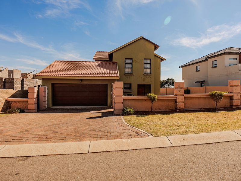 Front elevation of a two-story house featuring a tiled roof, integrated garage, and a brick-paved driveway with a perimeter boundary wall.