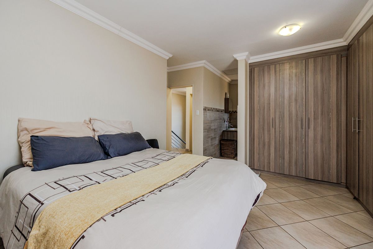 A well-maintained bedroom featuring built-in wooden cupboards, tiled flooring, and direct access to an en-suite bathroom area.