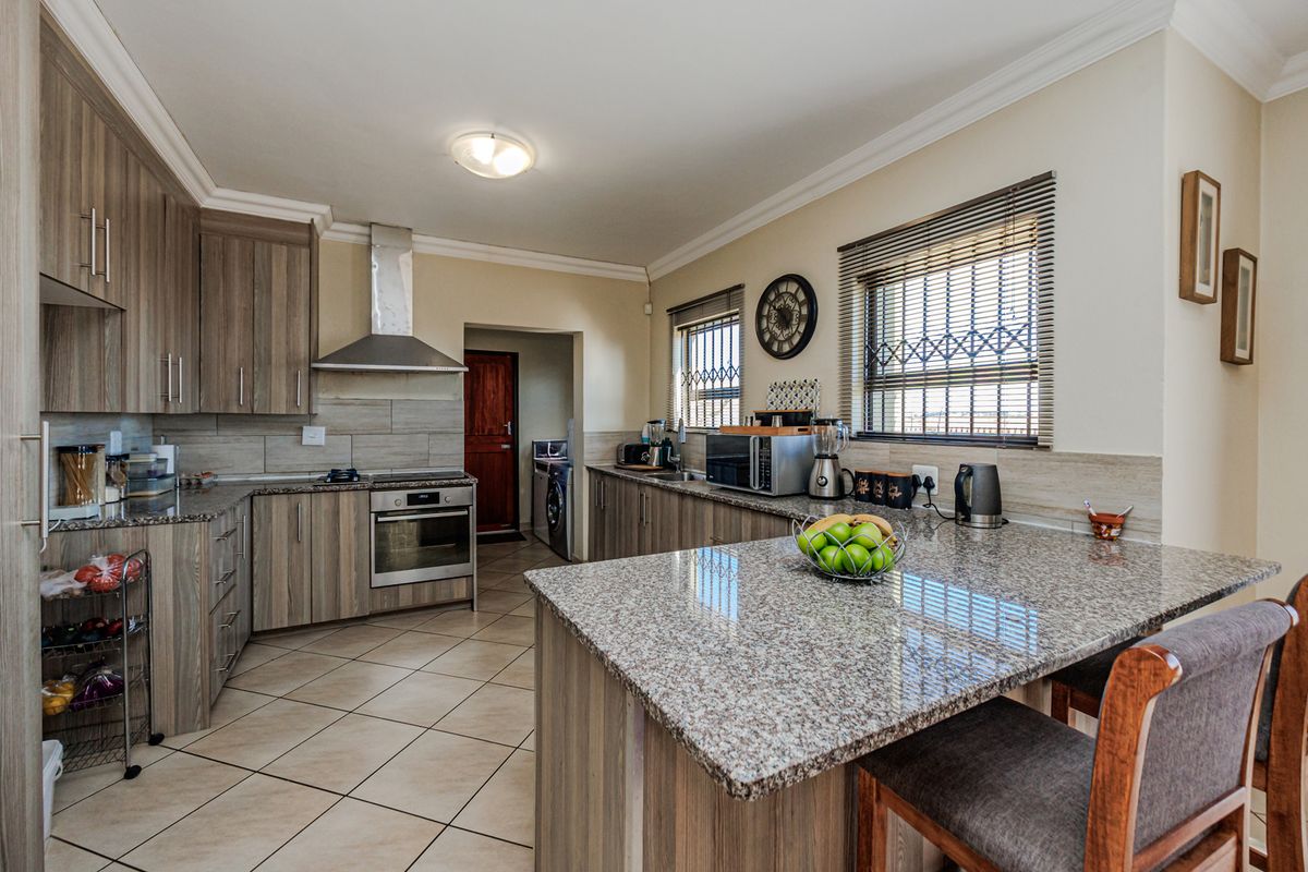A well-maintained kitchen featuring granite countertops, a central island, built-in oven with extractor fan, and tiled flooring with ample cabinetry.