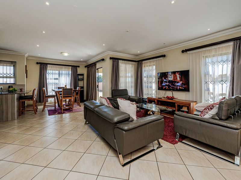 Spacious open-plan living and dining area featuring neutral ceramic floor tiles, recessed lighting, and a functional kitchen breakfast bar with granite countertops.