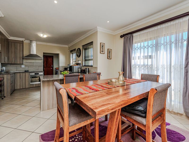 Open-plan kitchen and dining area featuring modern wood-finish cabinetry, granite countertops, built-in appliances, and tiled flooring with direct access to the patio.
