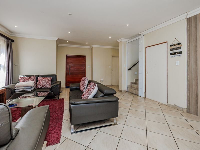 Spacious living room featuring neutral tiled flooring, recessed downlighting, and direct access to the front entrance and internal staircase.