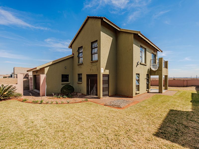 Rear view of a two-story residential house featuring a balcony, paved patio area, and a private garden with a lawn.