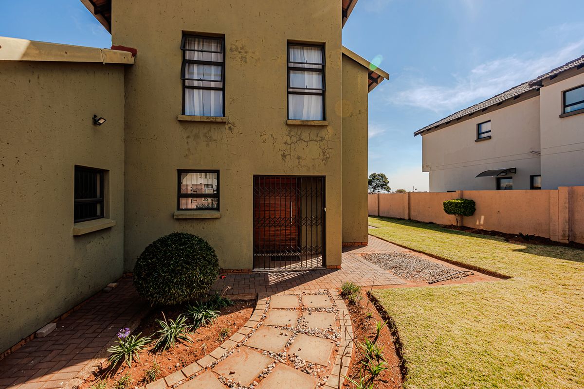 Rear view of the property featuring a paved walkway, lawn, boundary wall, and a secure entrance door with a metal security gate.