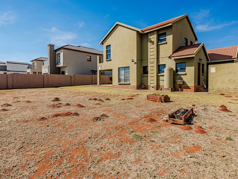 Rear view of the double-story house featuring a large backyard, perimeter wall, and installed water tank.