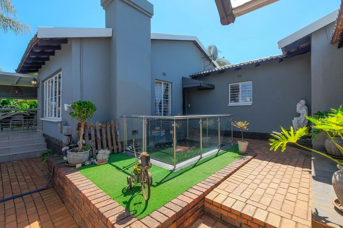 A well-maintained rear courtyard featuring brick paving, a glass-enclosed water feature, and a grey-painted exterior facade with a prominent chimney.