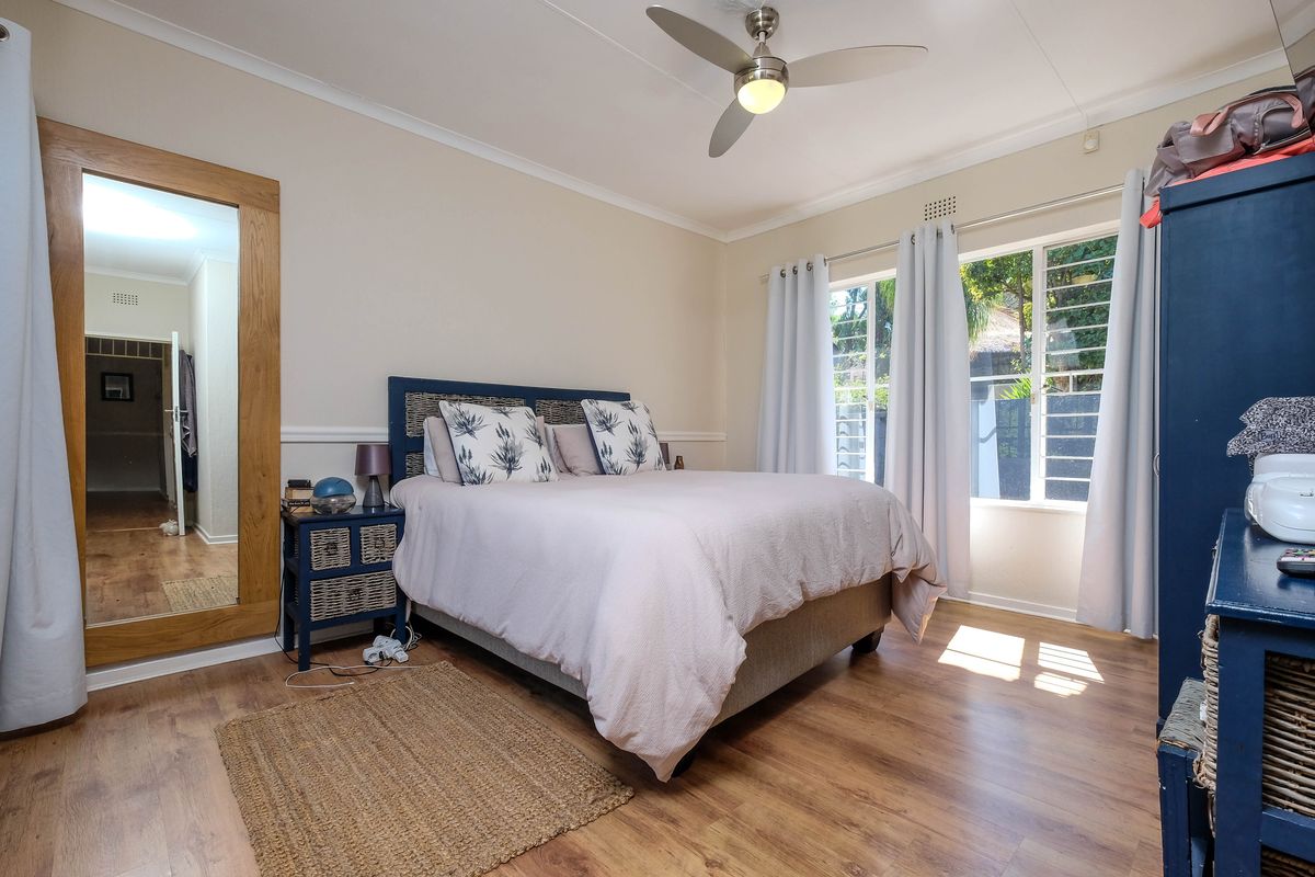 A well-lit bedroom featuring laminate flooring, a ceiling fan, and large windows with security bars, offering a comfortable and functional living space.