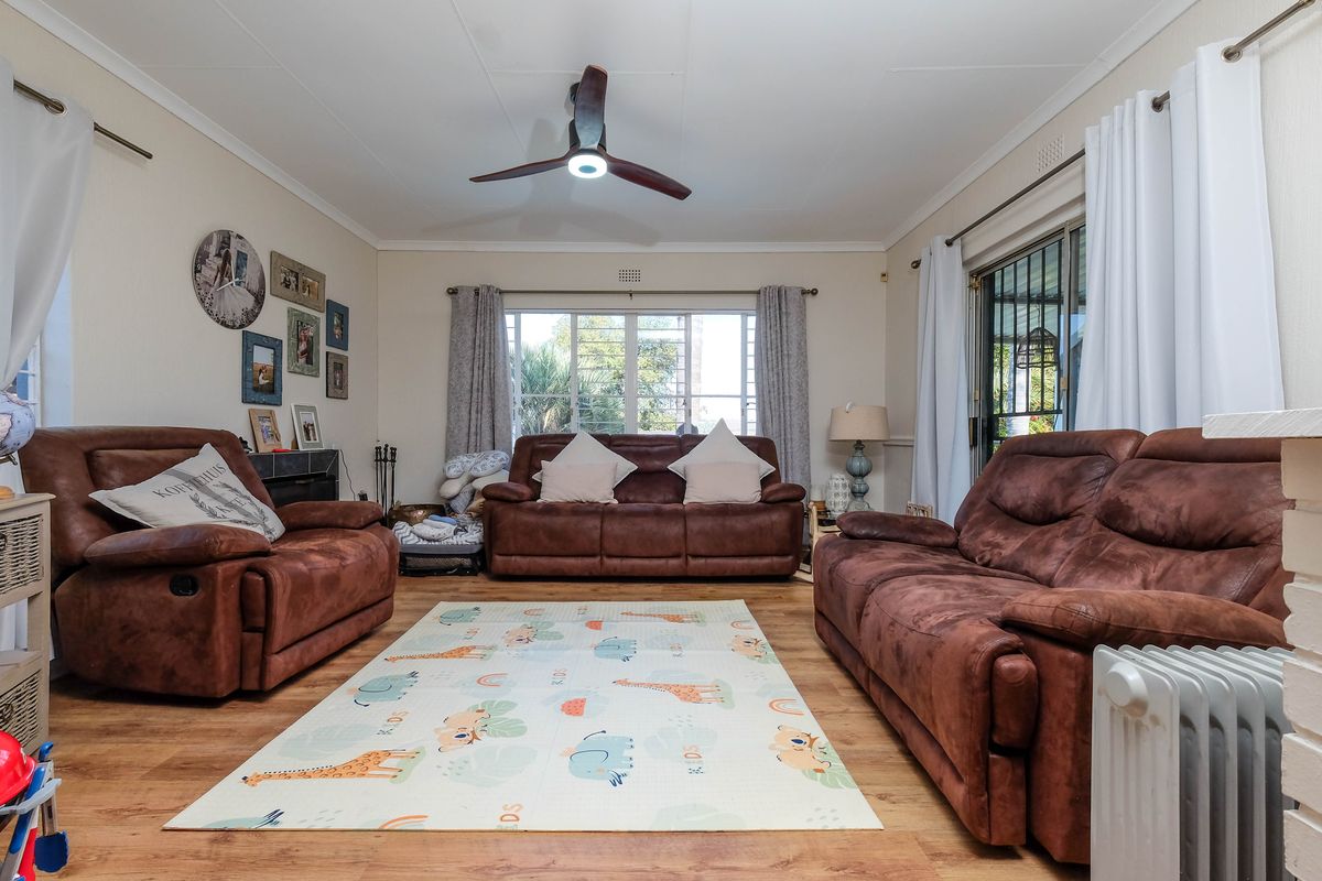 A comfortable living room featuring laminate flooring, a ceiling fan, and large windows providing natural light with access to the outdoor area.