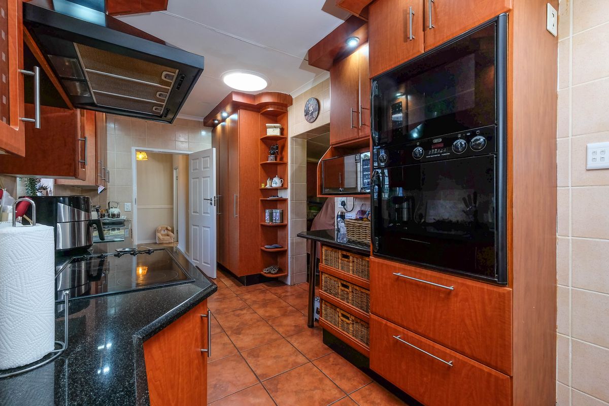 A functional kitchen featuring warm-toned wooden cabinetry, granite countertops, a built-in oven, and an electric hob with an overhead extractor fan.