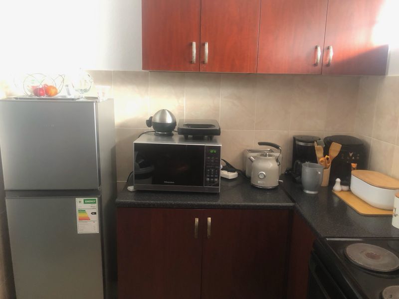 A compact kitchen area featuring dark wood-finish cabinetry, stone-look laminate countertops, and tiled splashbacks with an integrated electric hob.