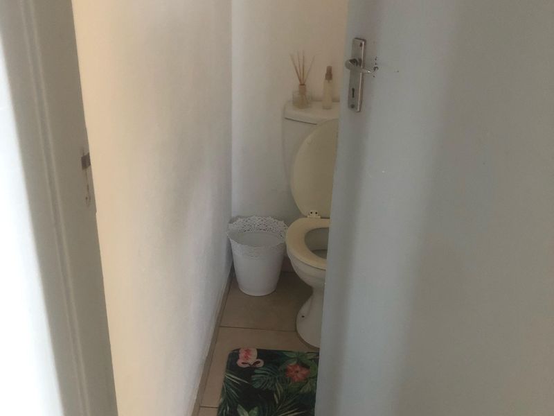 A compact bathroom featuring a standard toilet and tiled flooring, viewed through a partially open doorway.