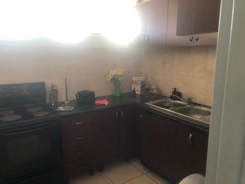 A compact kitchen featuring dark wood cabinetry, laminate countertops, a stainless steel sink, and a tiled backsplash.